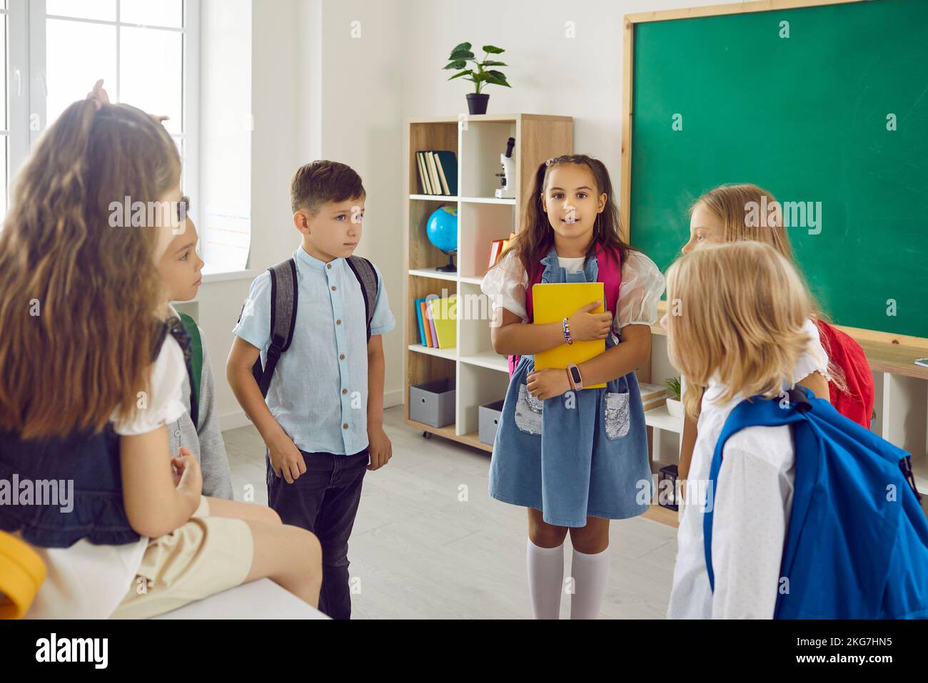 Les écoliers parlent ensemble en classe scolaire après les leçons tenant des chemises et des sacs. Banque D'Images