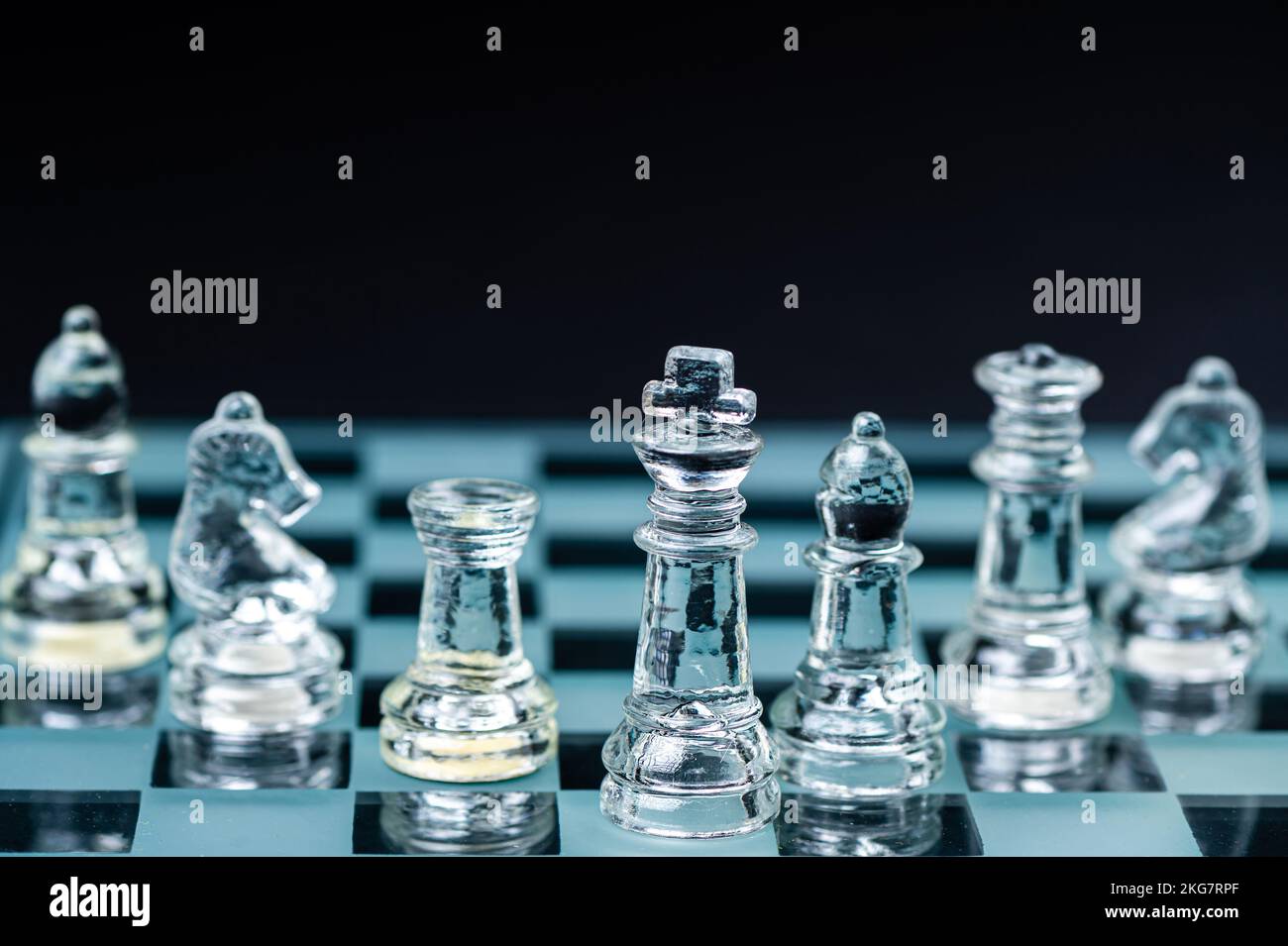 personnages d'échecs en verre transparent disposés en rangée et reflétant dans un échiquier en verre. Isolé sur le noir Banque D'Images
