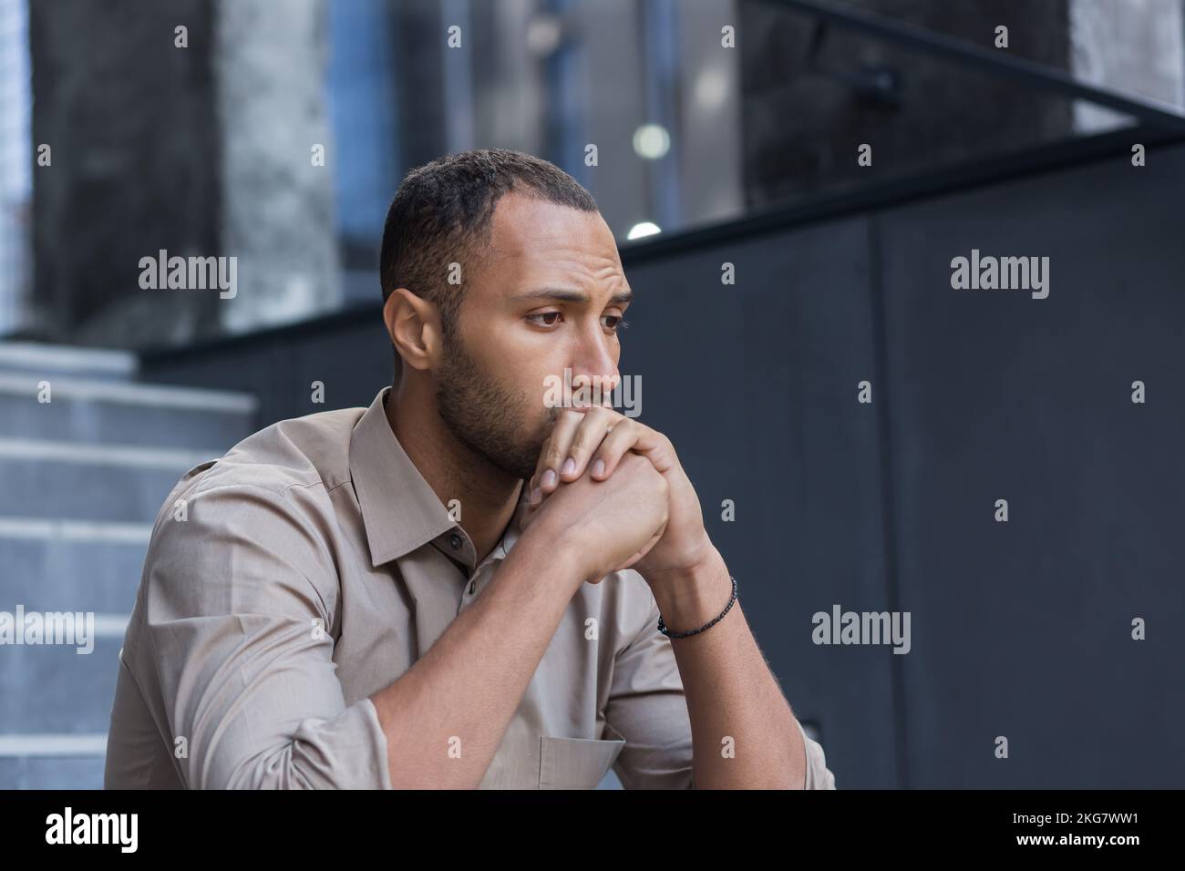 Portrait d'un homme hispanique.africain américain sérieux et triste. Il est assis sullenly dehors sur les escaliers, tient sa tête dans ses mains, regarde sur le côté. Banque D'Images