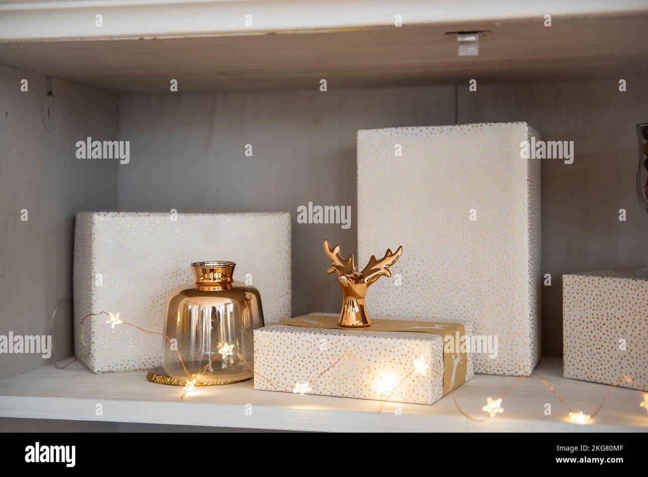 Derrière le verre d'une armoire avec vaisselle, les étagères sont décorées de jouets de Noël, guirlandes lumineuses, cadeaux dans un emballage rose. Jouets en forme de Banque D'Images