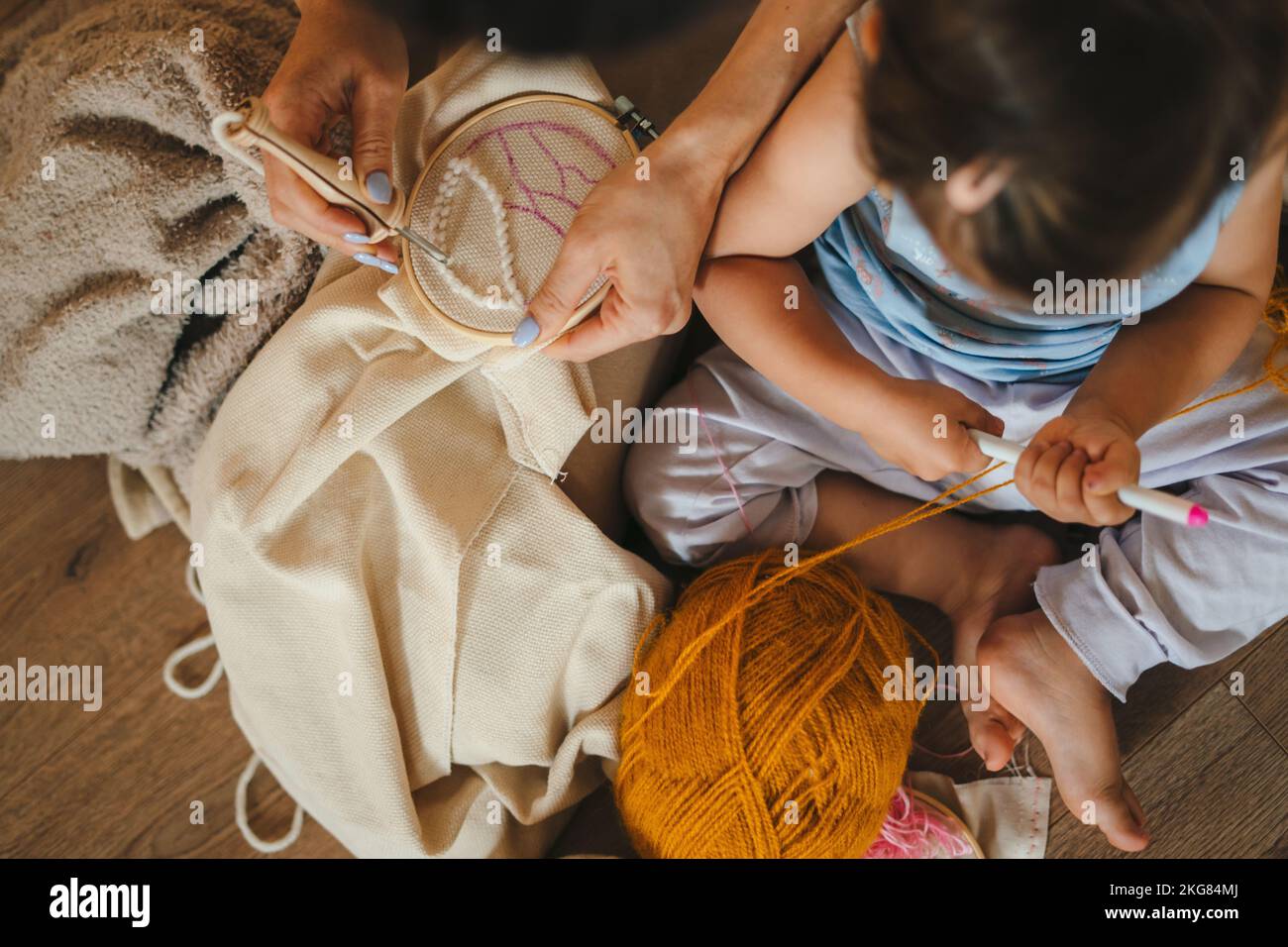 Vue de dessus d'une mère et d'une petite fille de bébé assis sur le sol dans le salon tricoter avec les aiguilles ensemble. Activité familiale à la maison. Personnes Banque D'Images