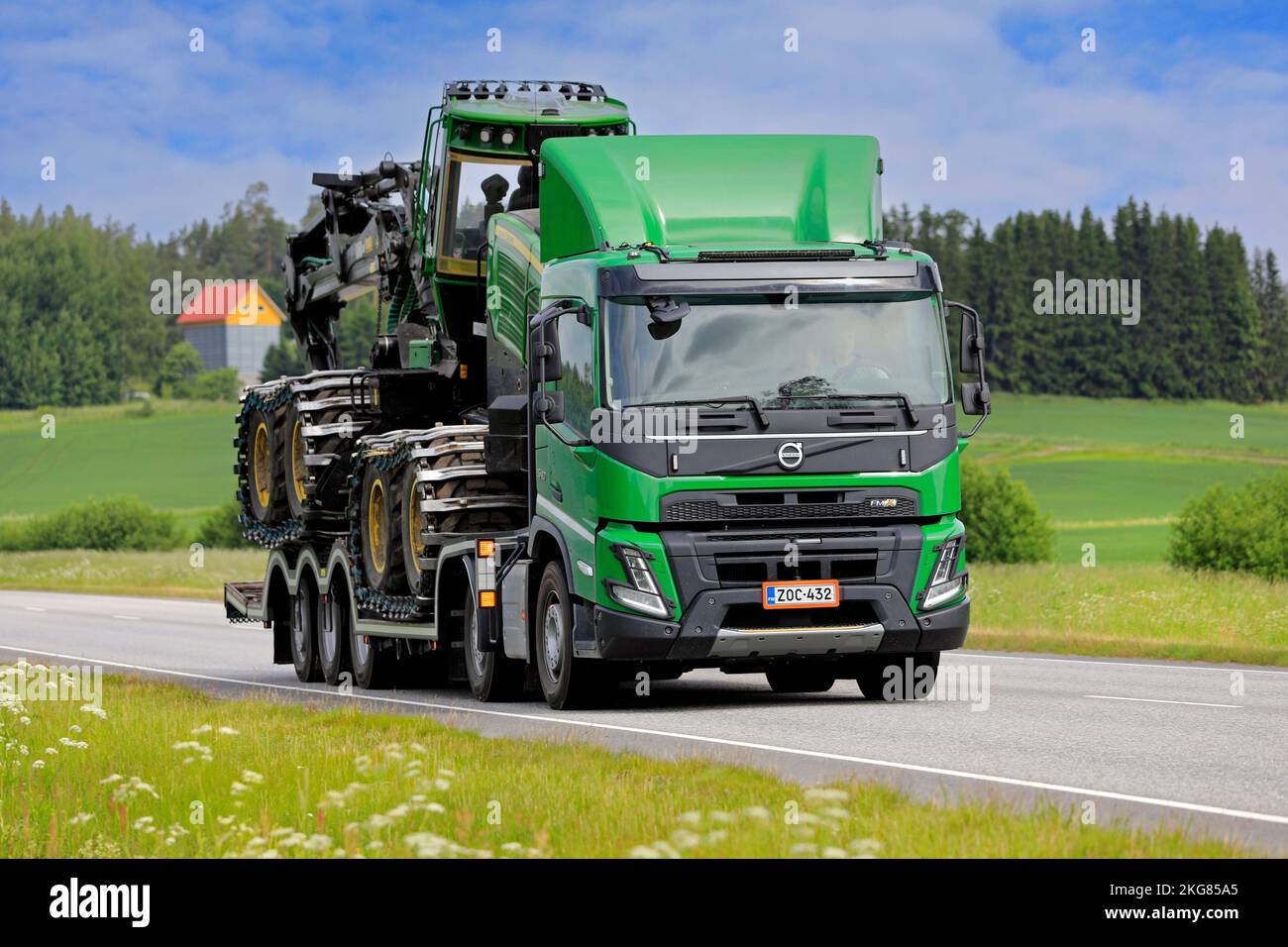Le camion FMX de Green Volvo transporte la récolteuse forestière John Deere sur une remorque le long de l'autoroute 52, lors d'une belle journée d'été. Salo, Finlande. 23 juin 2022. Banque D'Images