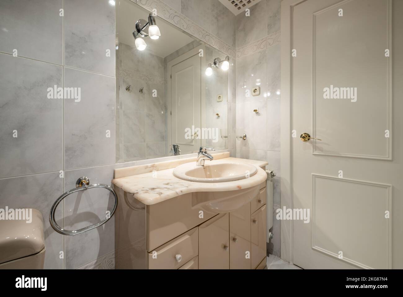 Salle de bains classique avec sanitaires crème, miroir biseauté intégré dans le mur avec porte en bois blanche Banque D'Images
