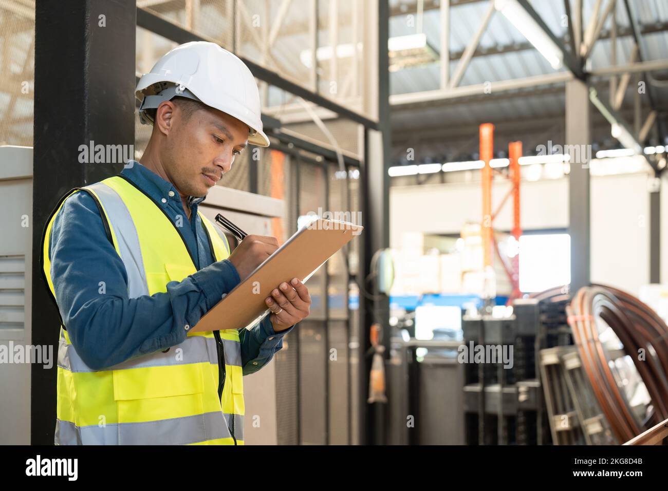 Homme asiatique portant une veste réfléchissante tenant le papier de liste de contrôle debout dans l'entrepôt de l'usine. Banque D'Images