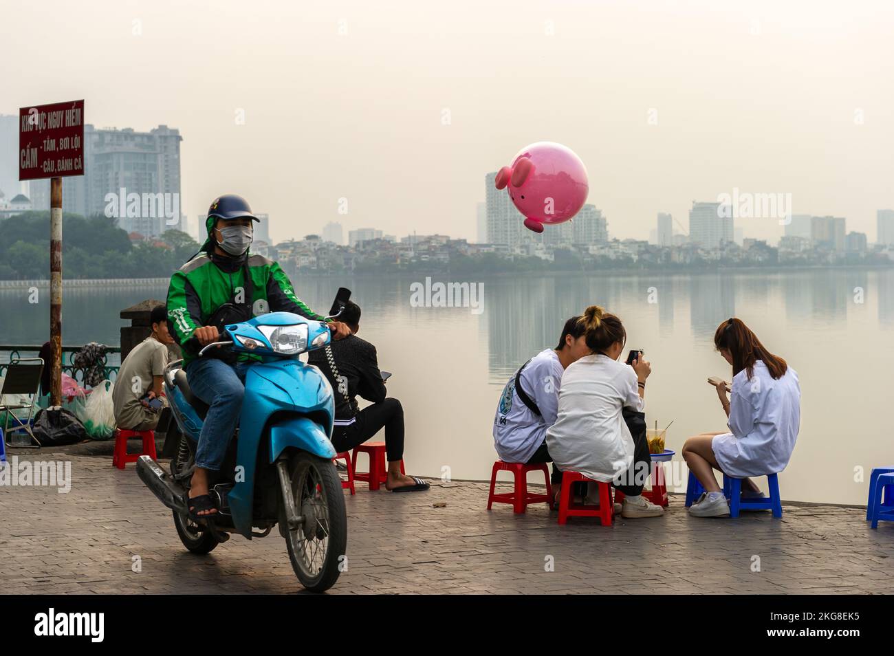 Amis se détendant au crépuscule près d'un misty Hồ Lac Tây, Hanoi, Vietnam Banque D'Images
