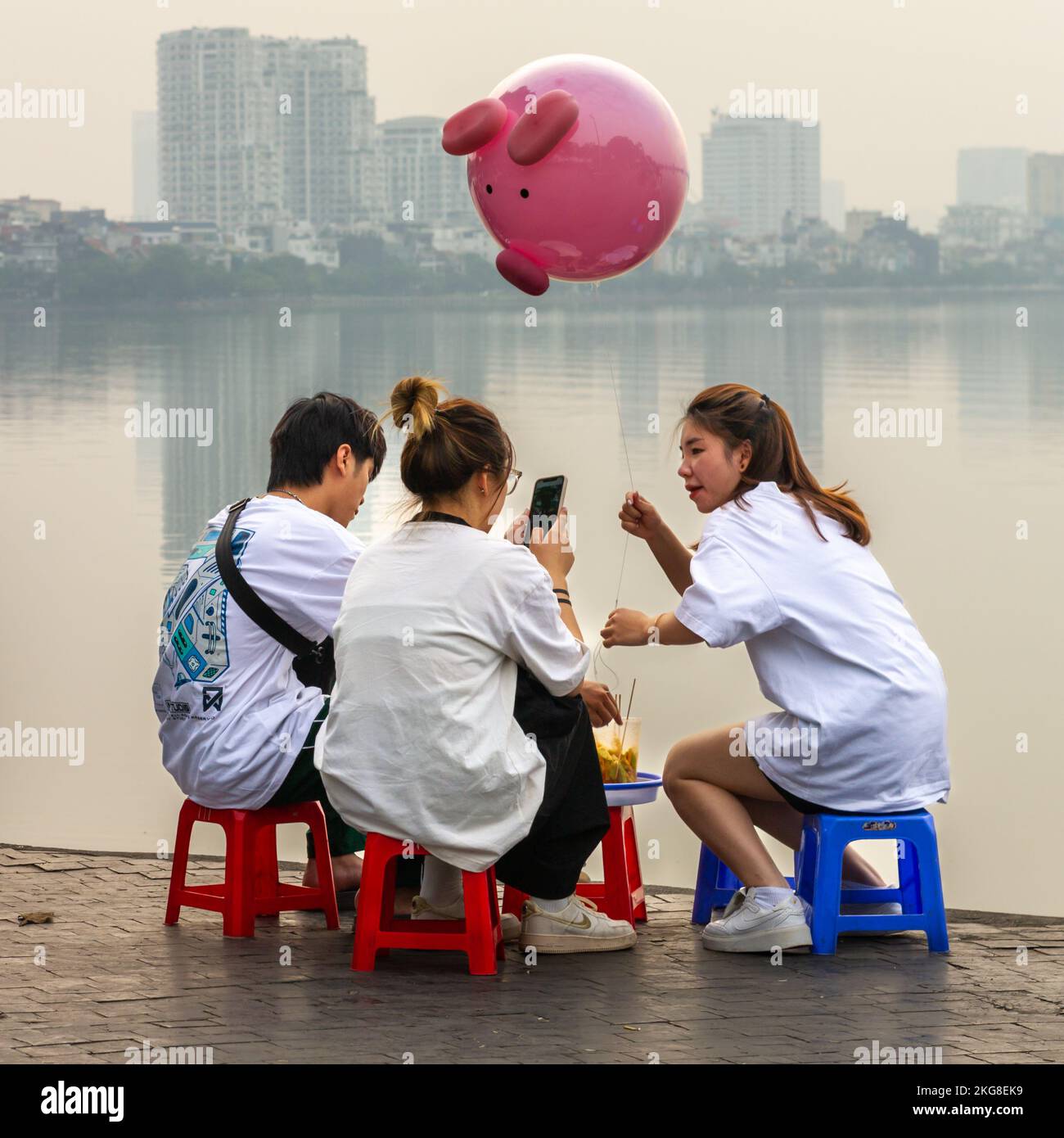 Amis se détendant au crépuscule près d'un misty Hồ Lac Tây, Hanoi, Vietnam Banque D'Images