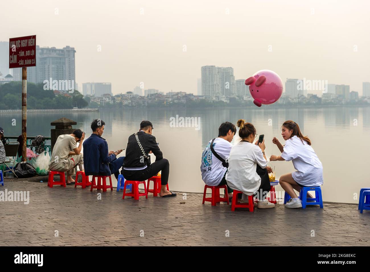 Amis se détendant au crépuscule près d'un misty Hồ Lac Tây, Hanoi, Vietnam Banque D'Images