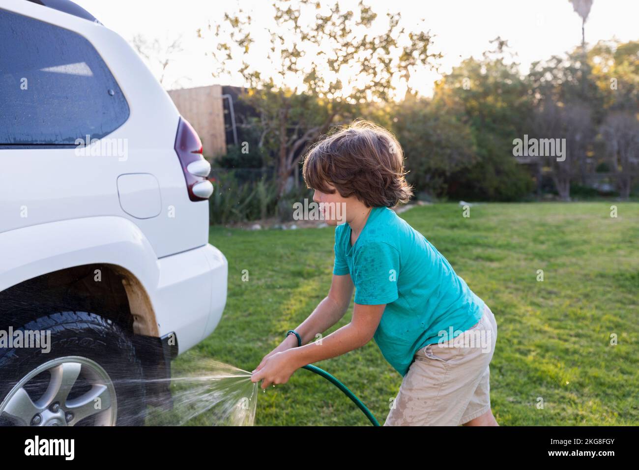Garçon (8-9) lavage SUV sur grande pelouse verte Banque D'Images