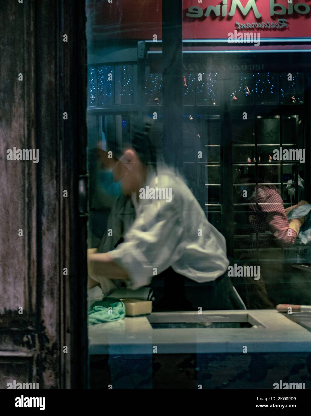 Une travailleuse dans un restaurant de Soho, Londres, effectuant une tâche, photographiée à travers une fenêtre avec de la condensation. Banque D'Images