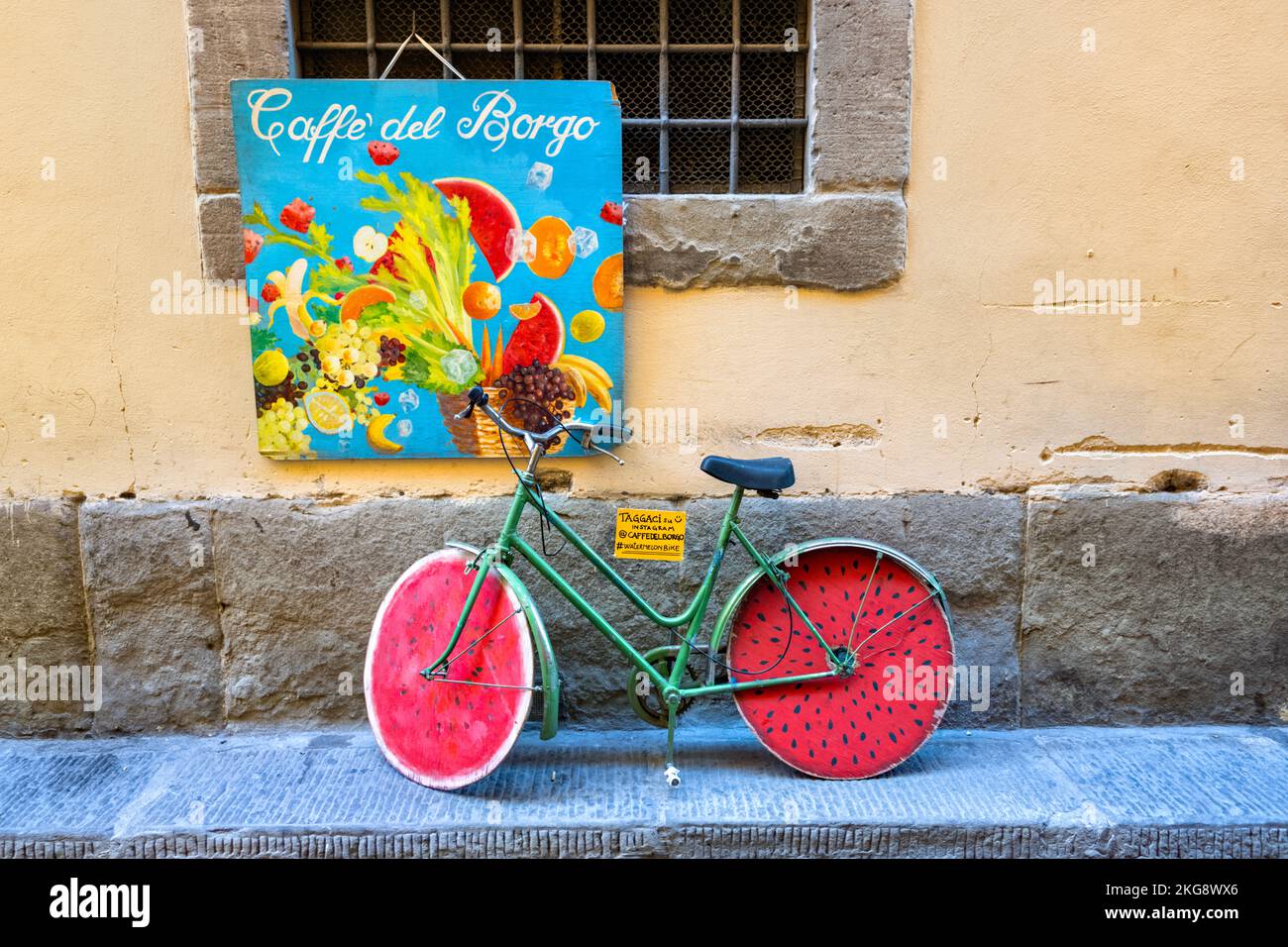 Vélo vert avec roues de pastèque rouges sous un panneau de couleur vive pour Caffe del Borgo, Florence, Italie Banque D'Images