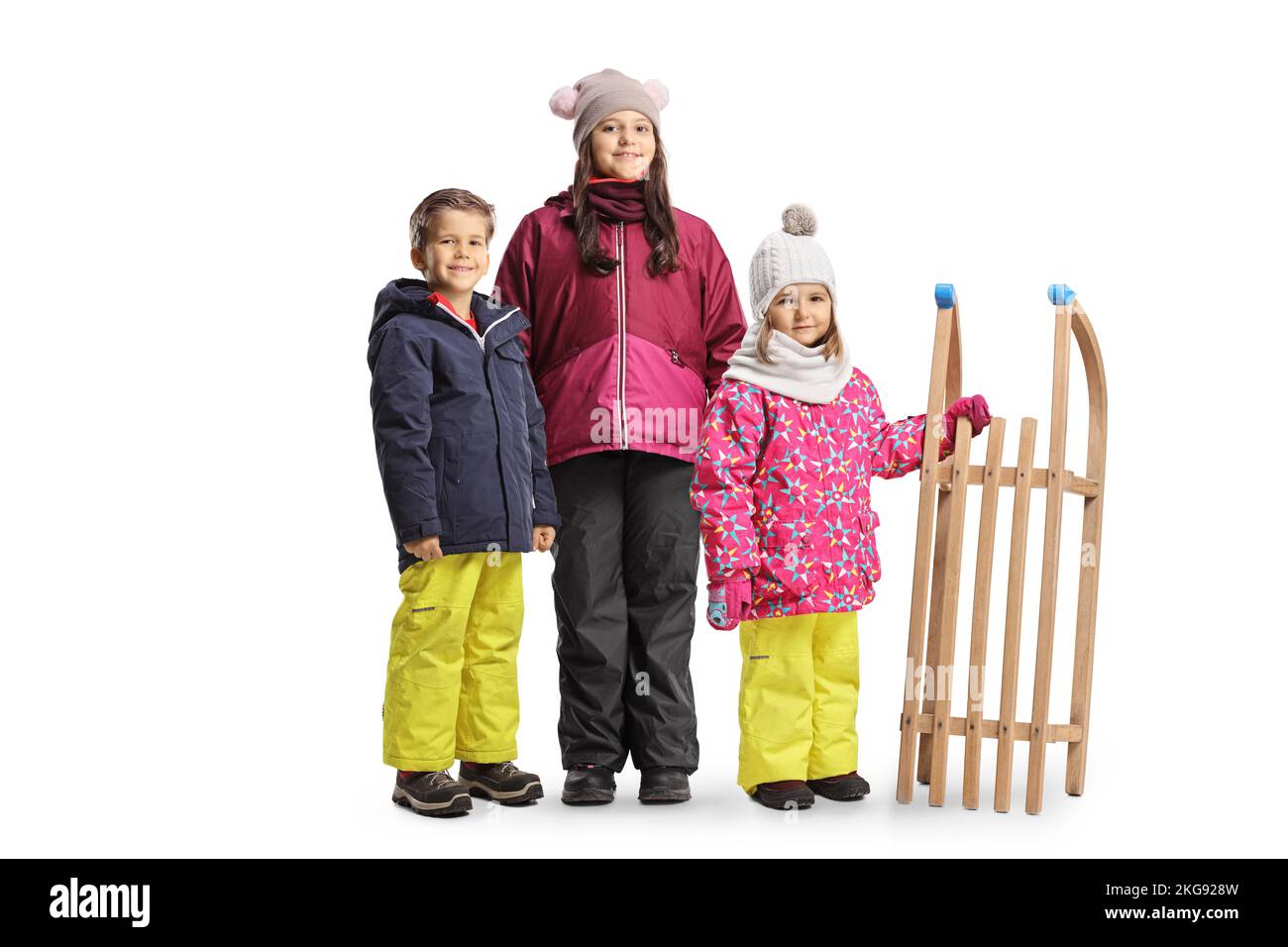 Deux filles et un garçon en vêtements d'hiver debout avec un traîneau en bois isolé sur fond blanc Banque D'Images