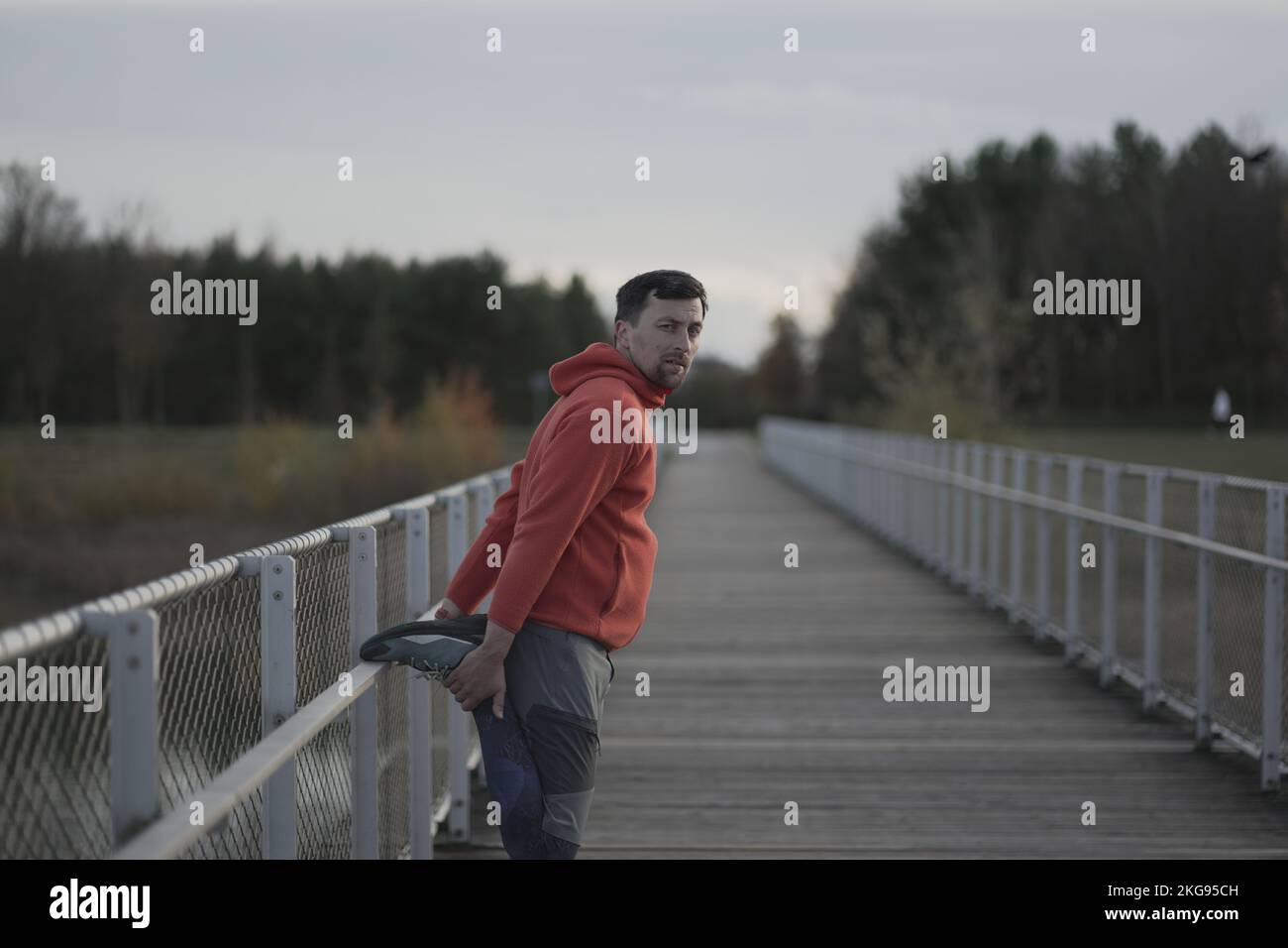 L'athlète s'échauffe avant un entraînement cardio-vasculaire en plein air. Un jogging réchauffe ses muscles pour un jogging dans la nature sur un pont en bois par temps froid d'automne Banque D'Images