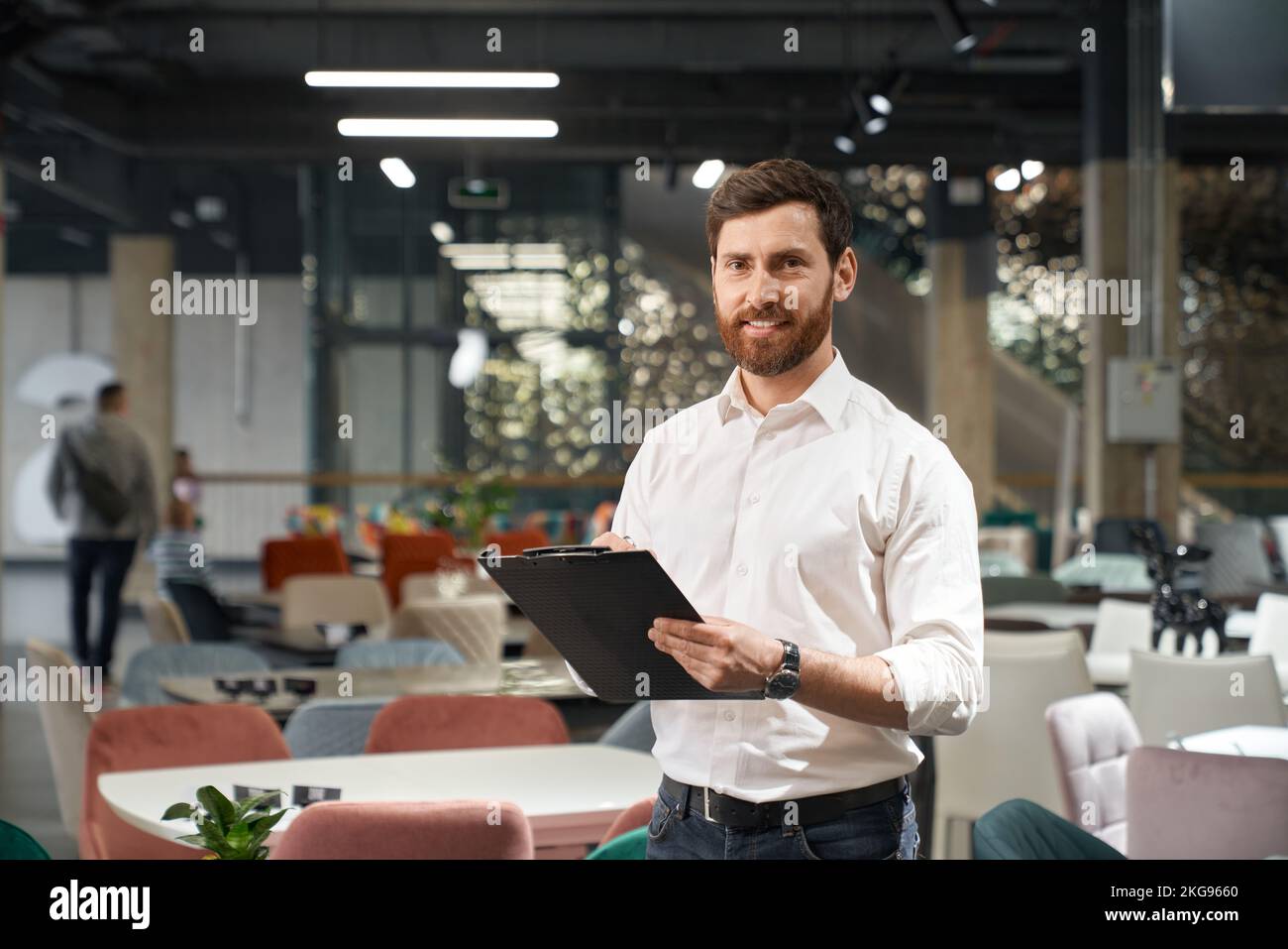 Entrepreneur réussi à porter des chemises pour faire des notes, tout en travaillant dans le centre d'exposition moderne. Portrait du beau restaurateur souriant à l'appareil photo, tout en choisissant des meubles dans le magasin. Concept d'entreprise. Banque D'Images