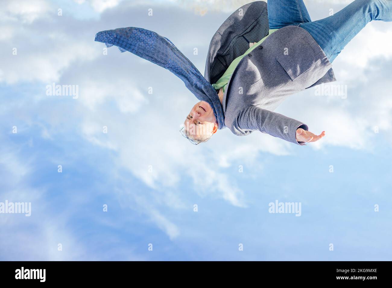 Image à l'envers d'un homme en veste et écharpe sautant haut et regardant l'appareil photo sur fond ciel nuageux. Aventure Banque D'Images