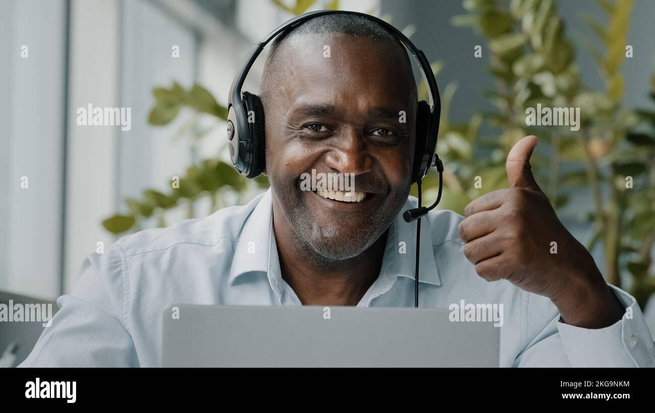 Un employé africain senior s'assoit au bureau portez un casque avec micro pour se connecter à la vidéoconférence. Appel professionnel sur ordinateur portable. Communication par webcam Banque D'Images