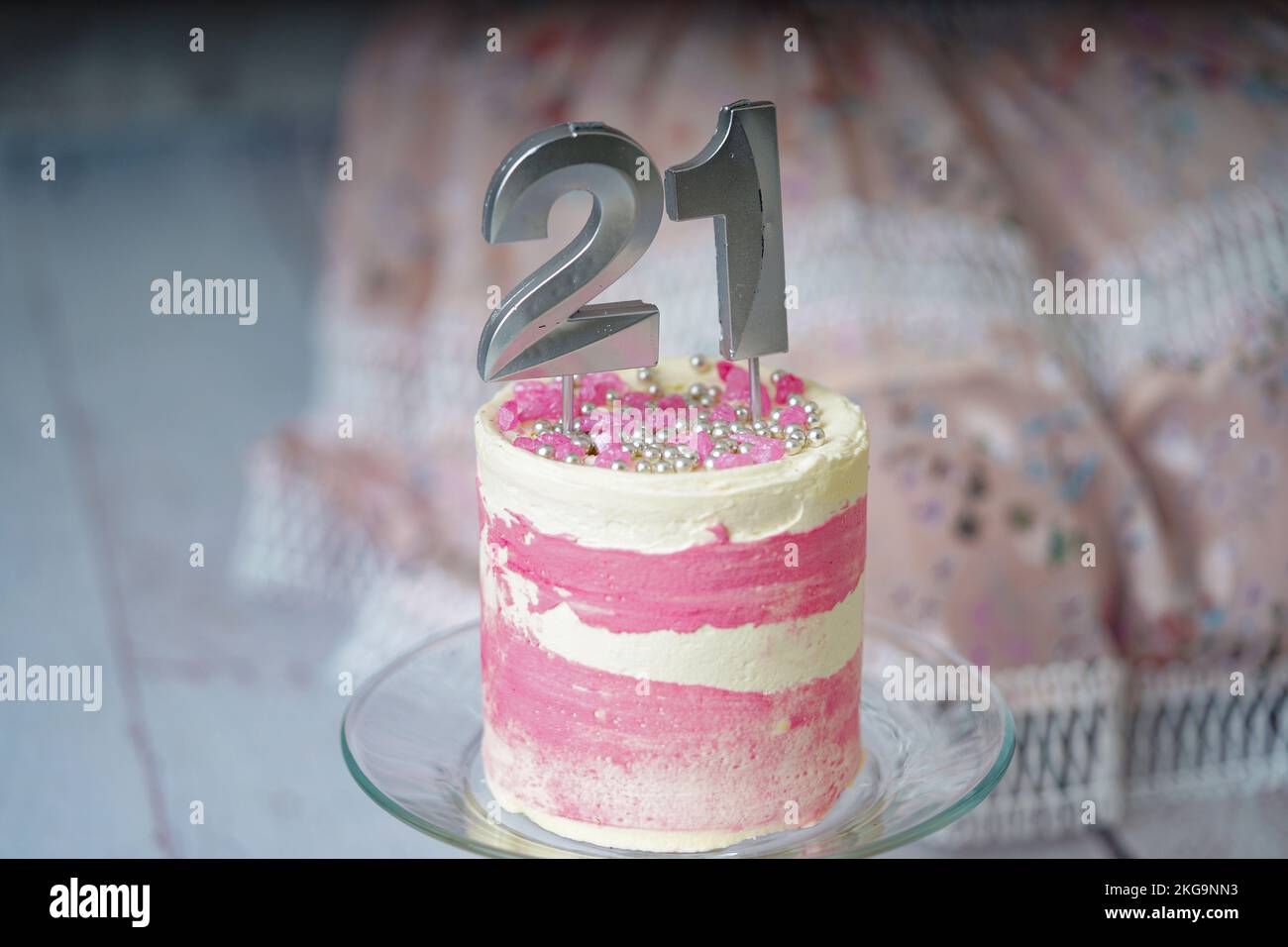 21st gâteau d'anniversaire gâteau rose et argent avec quelques saupoudres et 21st bougies avec une robe de femme à l'arrière-plan. Banque D'Images