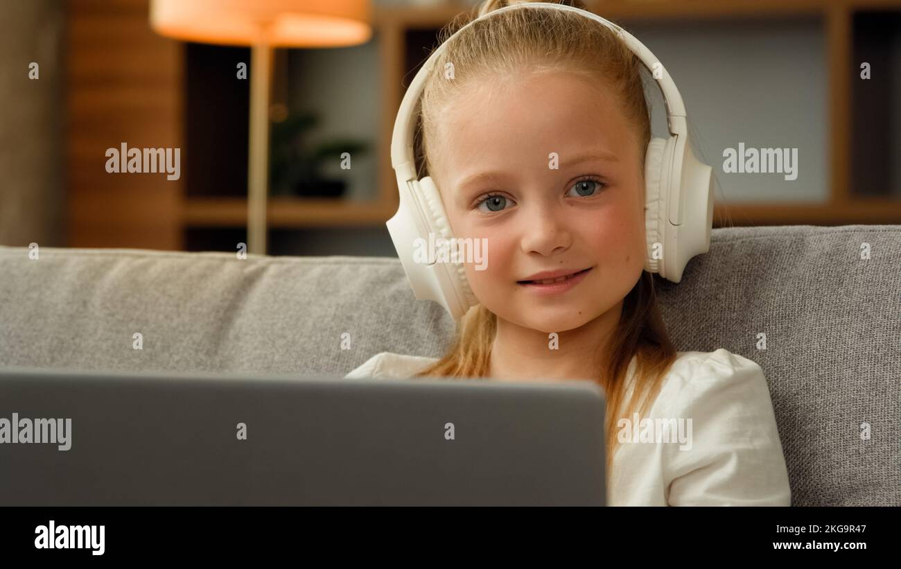 Adorable enfant heureux jolie fille dans les écouteurs s'asseoir à l'appartement écouter de la musique sur ordinateur portable jouer jeux d'ordinateur drôle petit enfant écofille montre tout-petit Banque D'Images