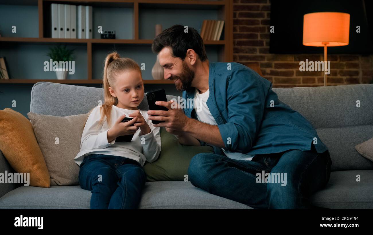 Caucasien homme et petite fille d'enfant s'assoient ensemble à la maison tenir téléphone moderne navigation contenu média jouer jeux en ligne papa adulte enseigner l'utilisation de fille d'enfant Banque D'Images