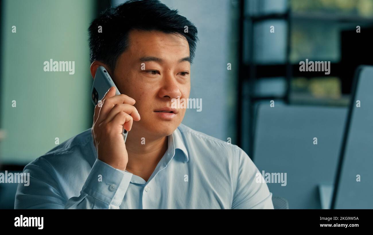 Triste homme d'affaires asiatique cadre homme d'affaires d'âge moyen coréen japonais chinois répondre appel mobile travail dans le bureau parler téléphone résoudre les affaires Banque D'Images