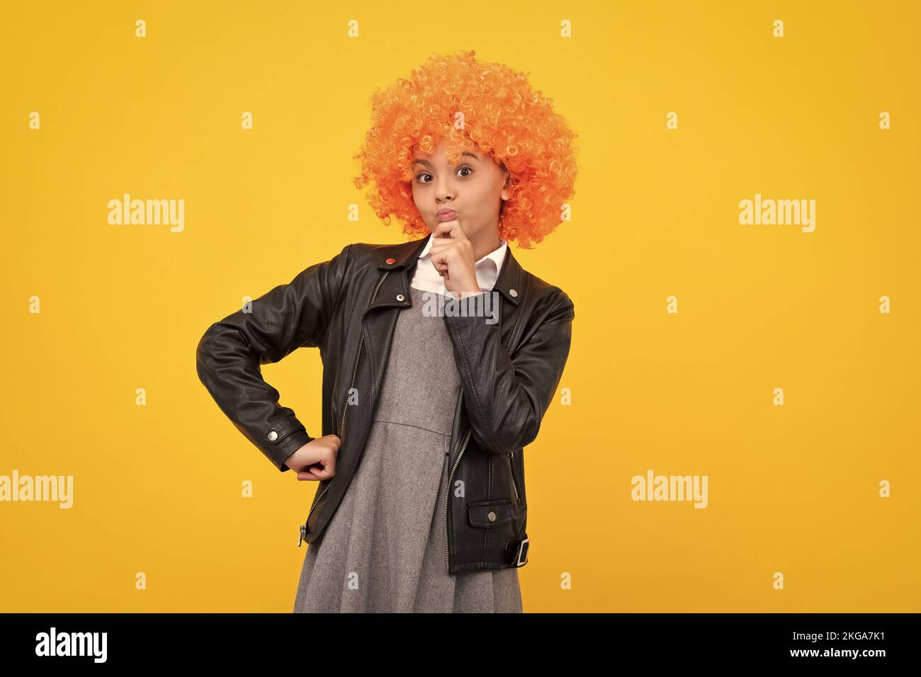 Enfant drôle avec perruque à cheveux bouclés. Jolie petite fille aux cheveux fantaisie. Enfant portant une perruque lumineuse à cheveux rouges. Penser face, émotions réfléchies de Banque D'Images