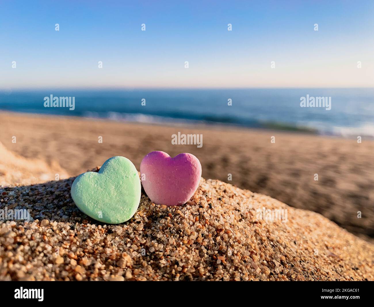 Gros plan de deux cœurs de bonbons sur une plage de sable avec l'océan au loin et le ciel bleu au-dessus Banque D'Images