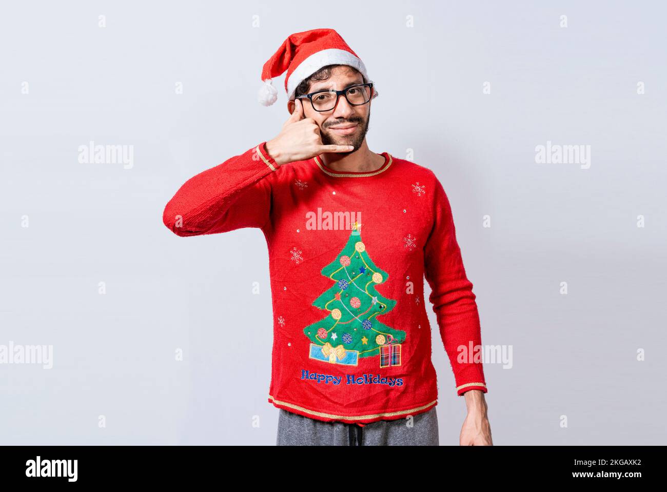 Les gens en vêtements de Noël faisant un geste d'appel avec leurs doigts. Homme en chapeau de noël imitant une conversation téléphonique, jeune homme latin en christma Banque D'Images