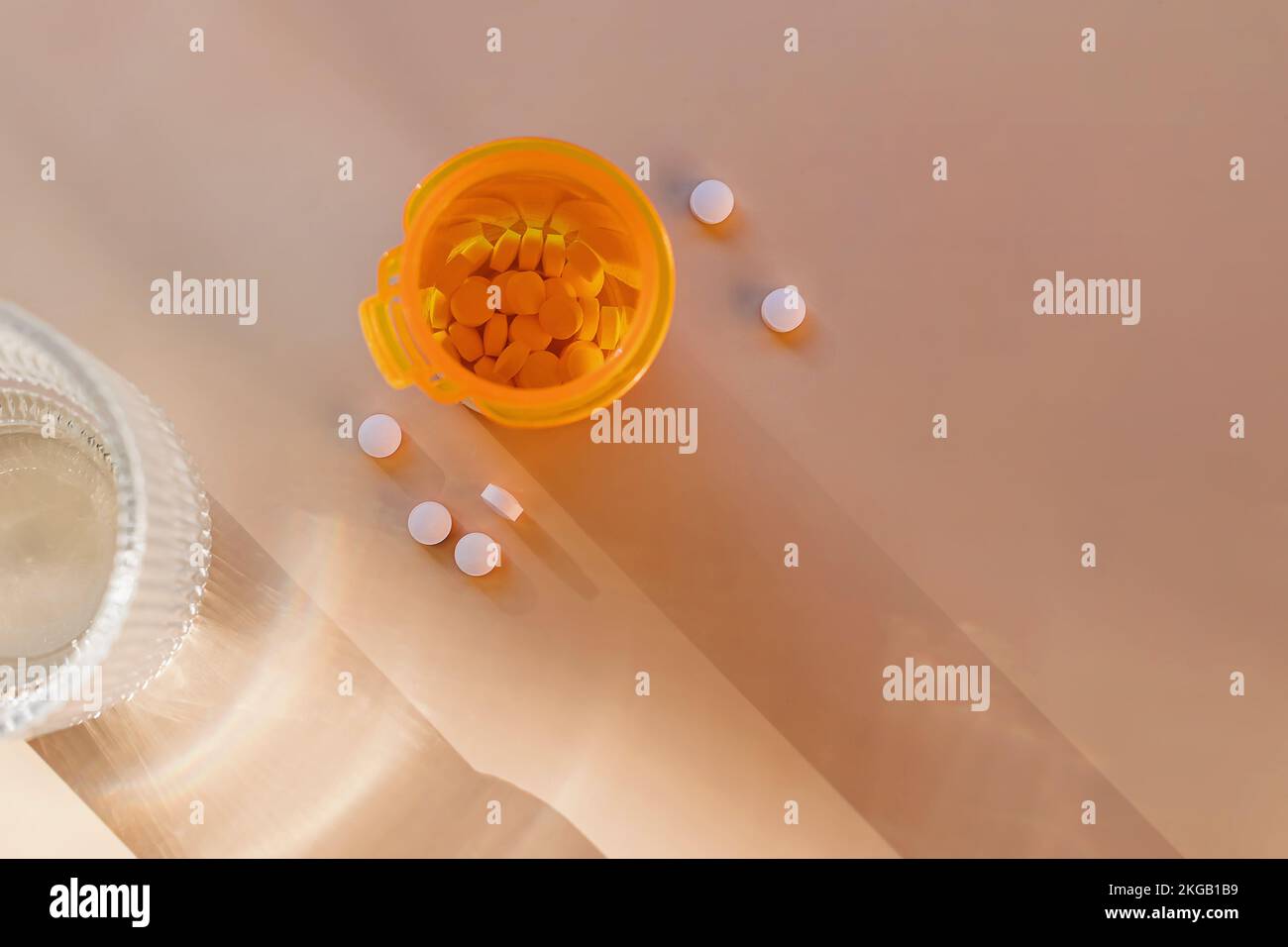 Pilules dans une bouteille en plastique orange et un verre d'eau, vue de dessus Banque D'Images