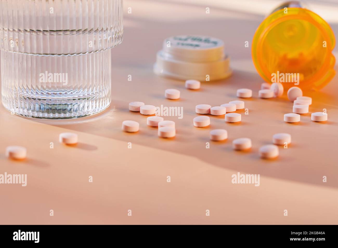 Gros plan des pilules dispersées sur la table, bouteille de médicament en plastique orange et verre d'eau. Mise au point sélective. Banque D'Images