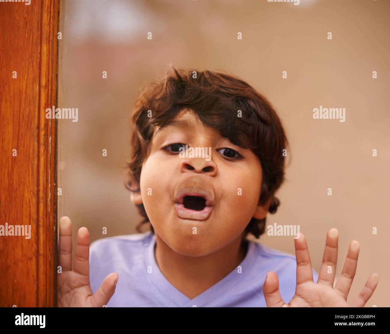 Regardez, je suis un poisson. Un petit garçon mignon tirant un visage contre une fenêtre en verre. Banque D'Images