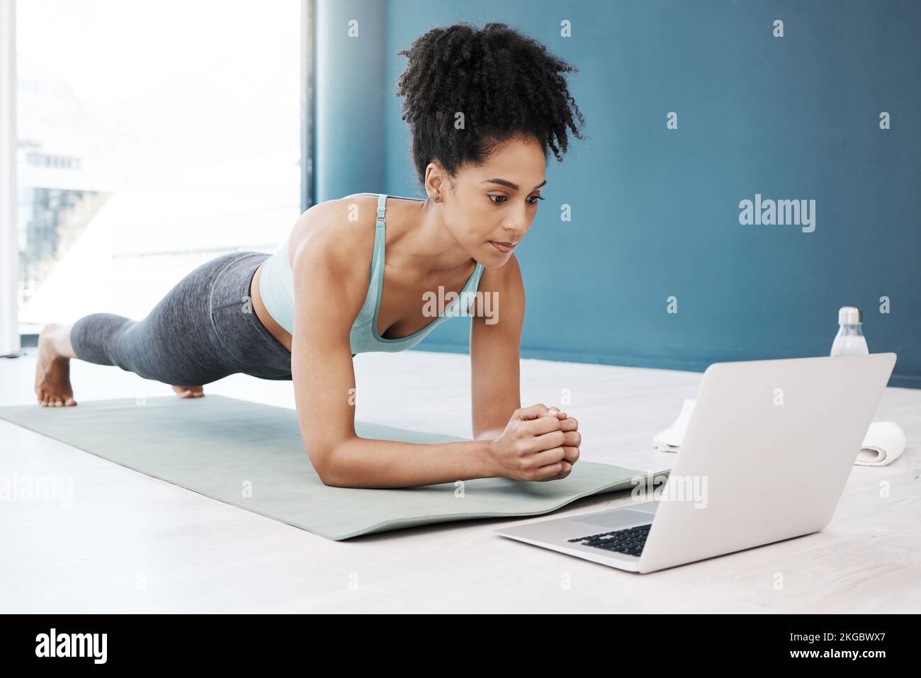 Séminaire en ligne sur le bien-être, le fitness et le yoga sur ordinateur portable pour femme noire en bonne santé et jeune en position de planche corporelle. Concentration, équilibre et conscience en ligne dans Banque D'Images