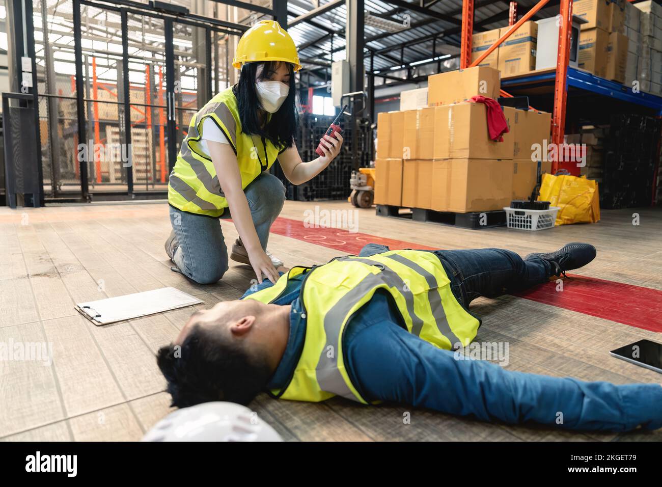 Une travailleuse d'entrepôt utilisant un talkie-walkie a appelé l'équipe de premiers secours de l'usine pour sauver un homme inconscient. laissez-passer ou rideaux occultants, dangereux Banque D'Images
