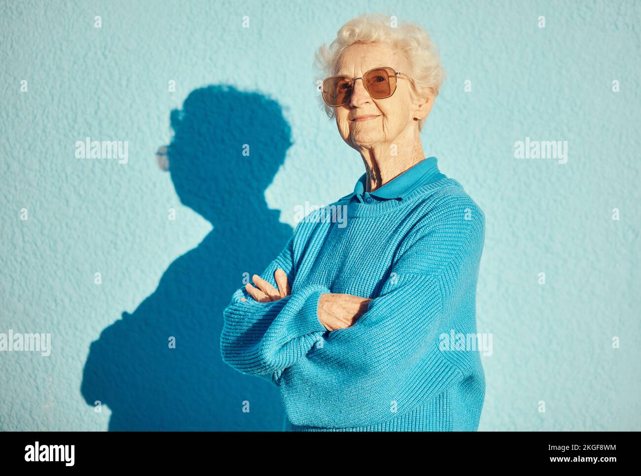 Mode, lunettes de soleil et portrait de la vieille femme avec les bras croisés sur le fond du mur pour un style, frais et esthétique unique. Retraite, beauté et Banque D'Images