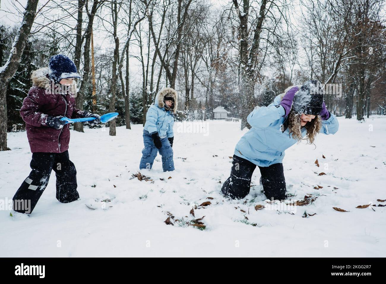 Famille heureuse, amis, mère et enfants s'amuser en plein air en hiver, fond de nature enneigée. Maman et deux garçons jouant au boules de neige à l'extérieur du parc hivernal Banque D'Images