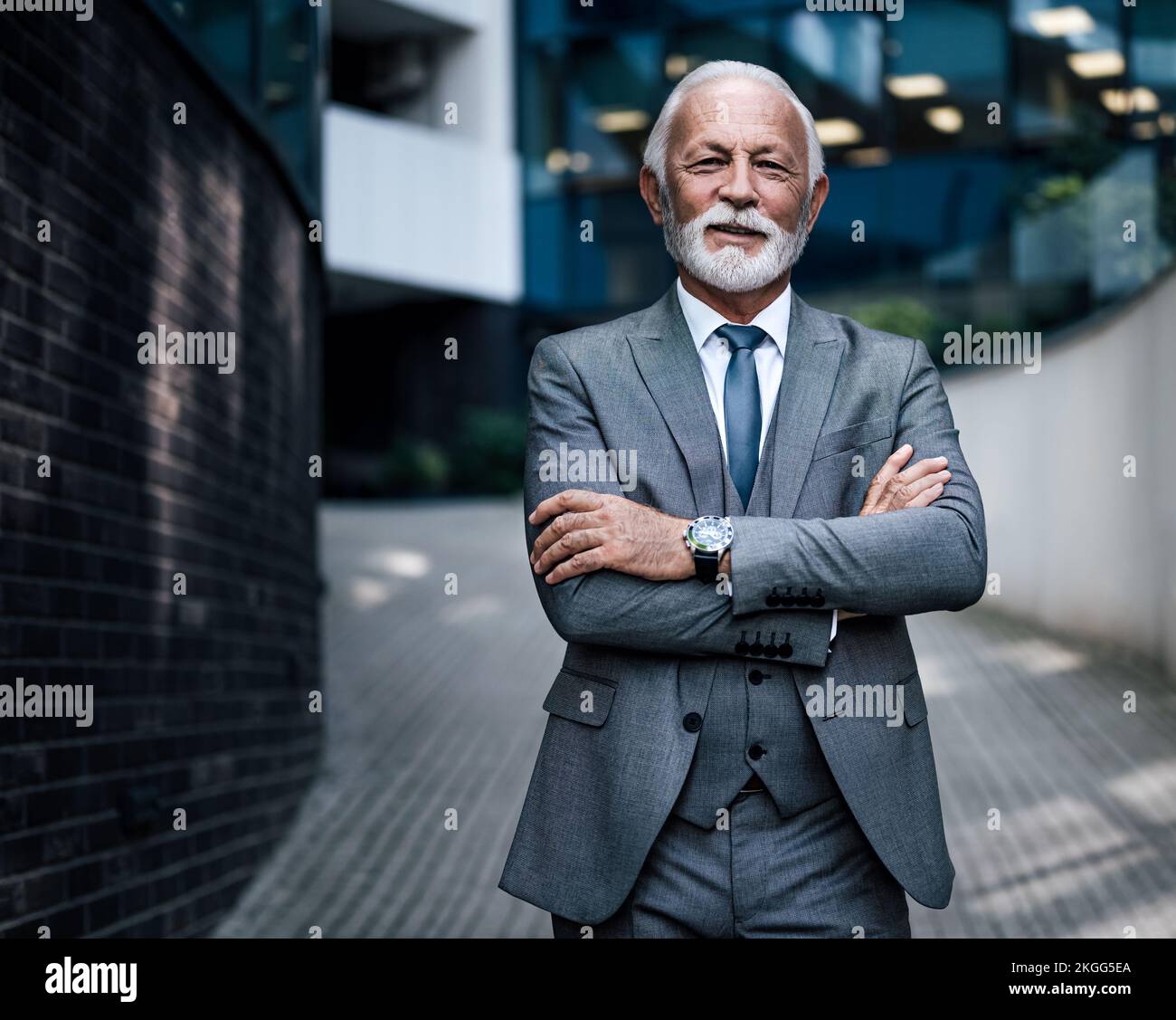 Portrait d'entrepreneur âgé confiant avec les bras croisés. Un homme d'affaires souriant se trouve sur une passerelle piétonne à l'extérieur d'un immeuble de bureaux moderne Banque D'Images