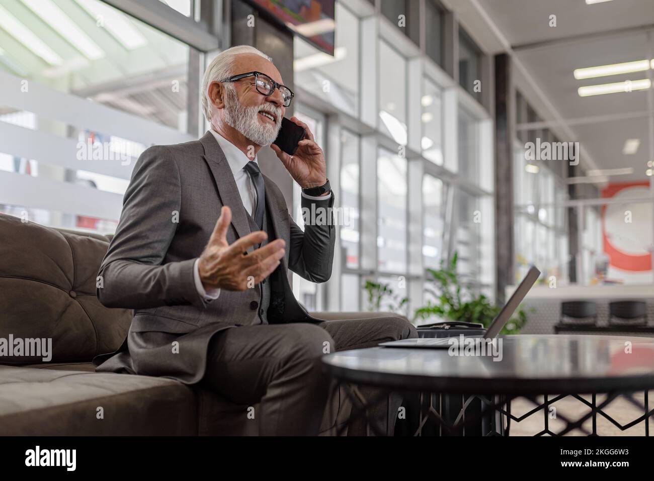 Homme d'affaires souriant entrepreneur parlant sur téléphone portable tout en utilisant l'ordinateur portable dans le bureau. Banque D'Images