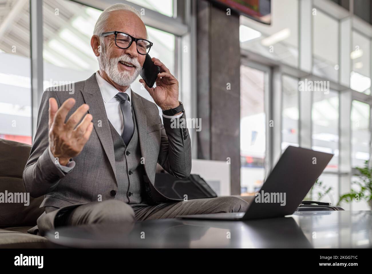 Un professionnel de la personne âgée qui parle avec succès sur un téléphone portable. Un homme d'affaires travaille sur un ordinateur portable tout en étant assis à la table. Il porte une combinaison complète Banque D'Images