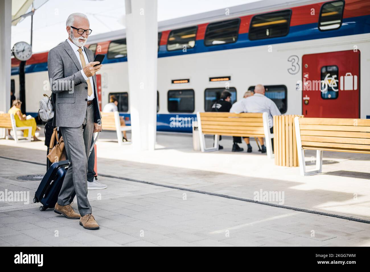 Messagerie professionnelle senior sur smartphone. Un homme d'affaires âgé marche avec une valise à la station de métro ou de train. Banque D'Images
