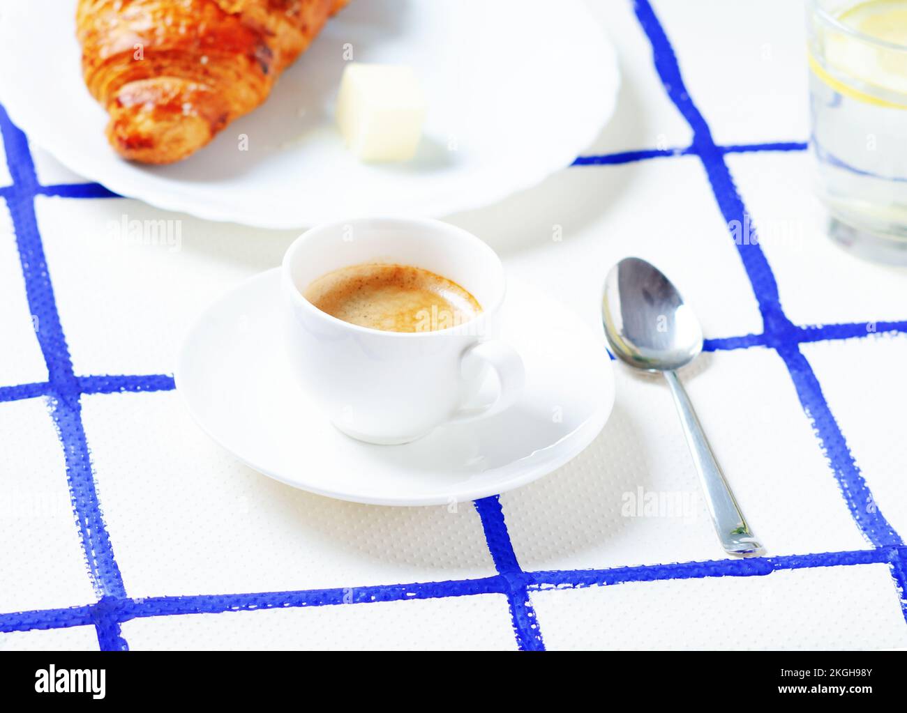 Une tasse de café blanc avec croissant et beurre sur fond à carreaux. Banque D'Images