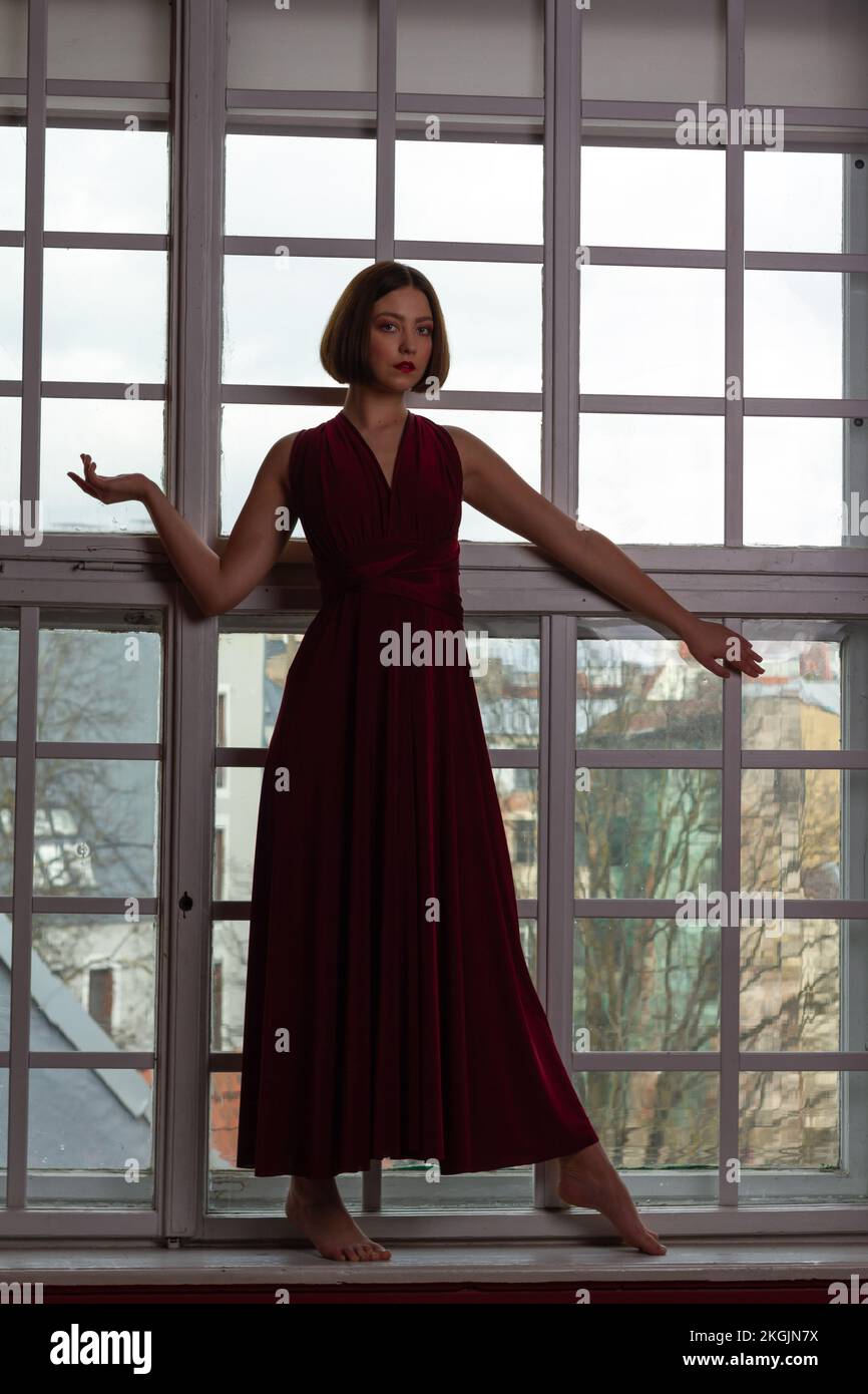 Une femme vêtue d'une robe rouge avec bras étendu devant une petite fenêtre de panneau Banque D'Images