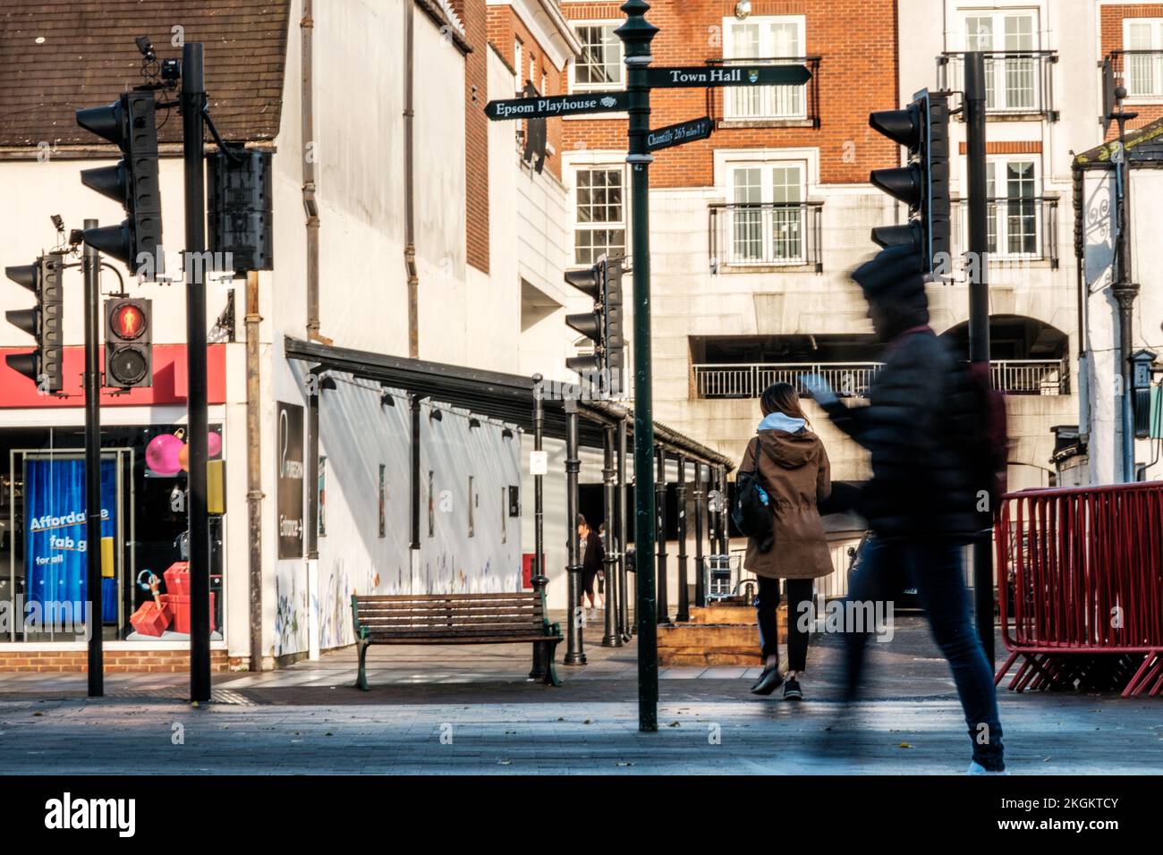 Epsom, Surrey, Londres, Royaume-Uni, 20 novembre 2022, femme Croossing Road Man marchant à l'aide d'un téléphone mobile ou d'un smartphone sur Une rue du centre-ville de High Street Banque D'Images