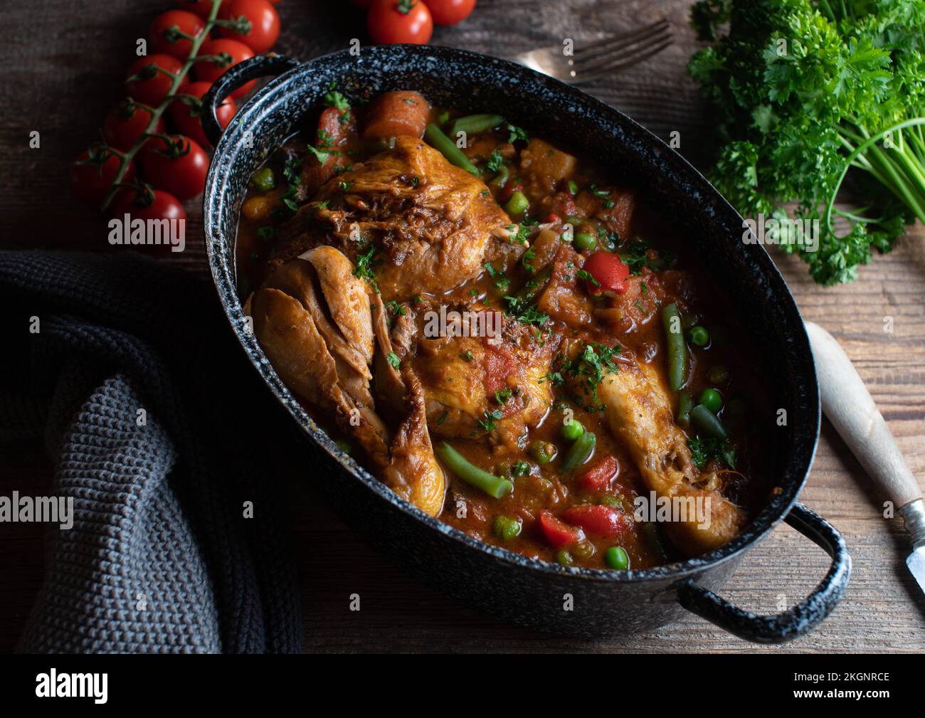 Ragoût de poulet brun avec légumes, pommes de terre et légumineuses dans un pot à l'ancienne sur table en bois Banque D'Images