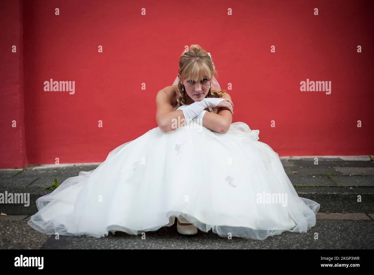 Allemagne, Rhénanie-Palatinat, portrait of bride sitting on curb en face de façade rouge Banque D'Images