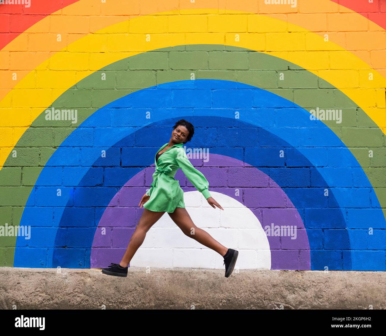 Femme sautant devant le drapeau arc-en-ciel peint sur le mur Banque D'Images