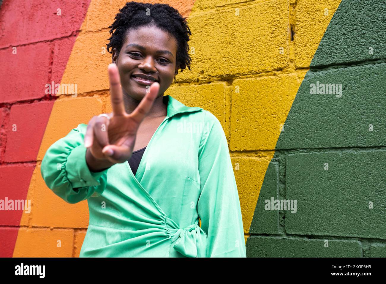 Jeune femme souriante gestante signe de paix devant un mur coloré Banque D'Images