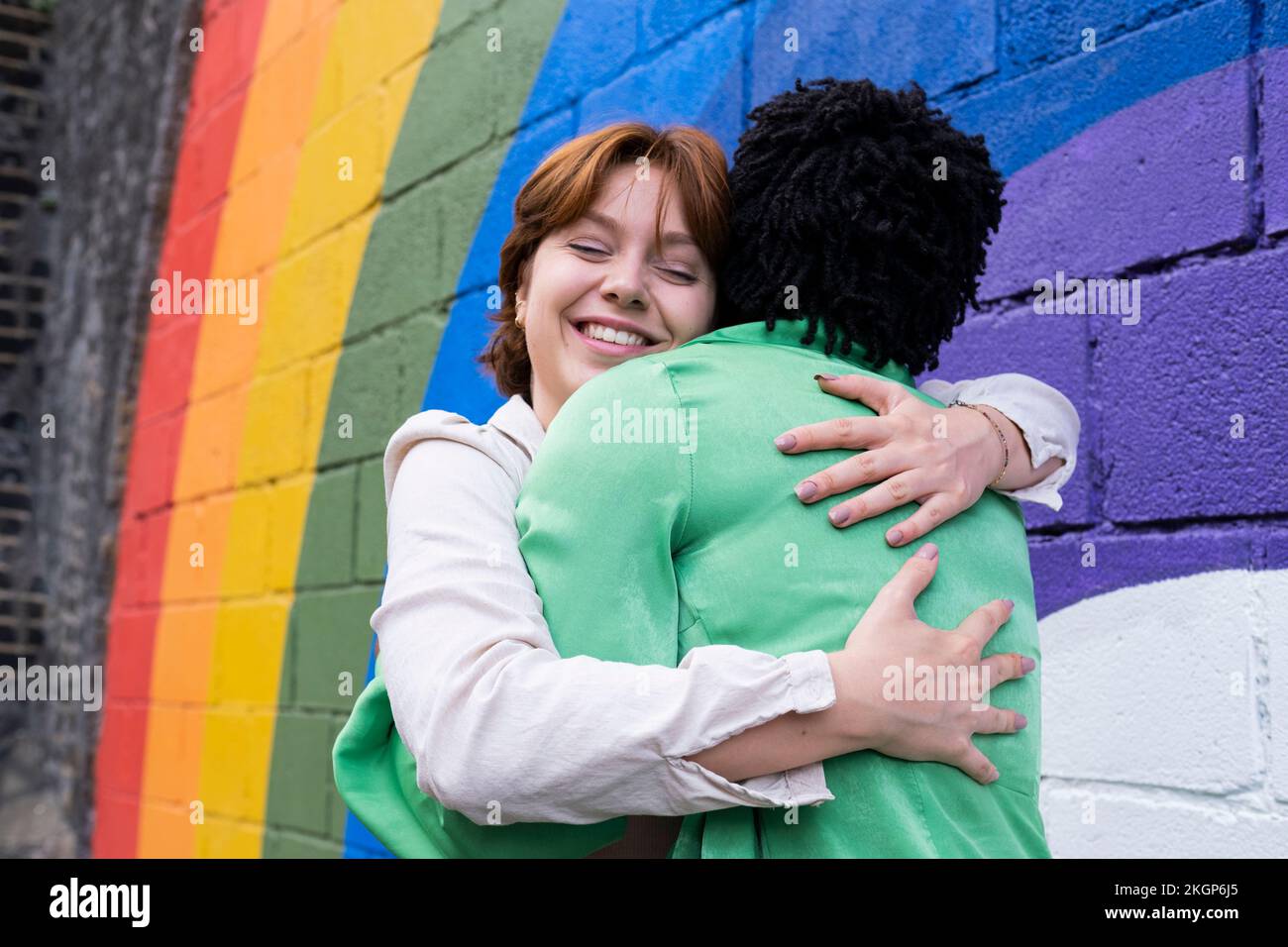 Femme souriante embrassant l'ami par le drapeau arc-en-ciel peint sur le mur Banque D'Images