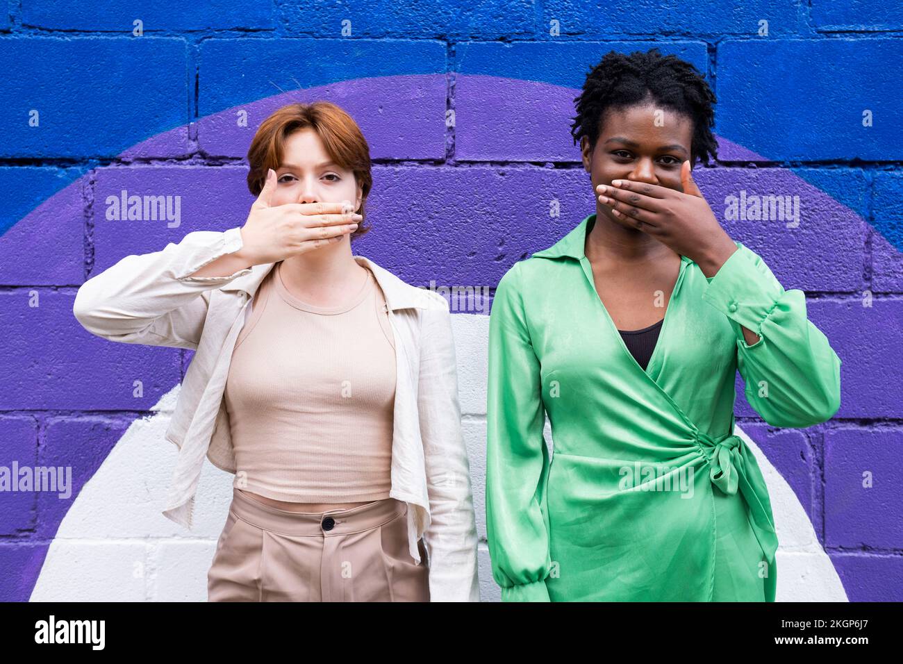 Des amies féminines couvrant la bouche avec les mains devant le mur coloré Banque D'Images
