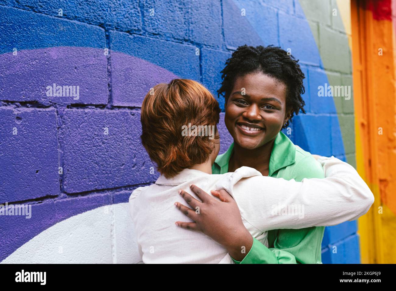Femme souriante embrassant un ami par un mur coloré Banque D'Images