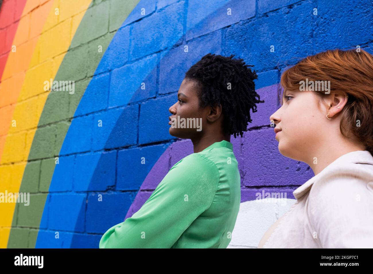 Femme réfléchie avec un ami par un mur de couleur arc-en-ciel Banque D'Images