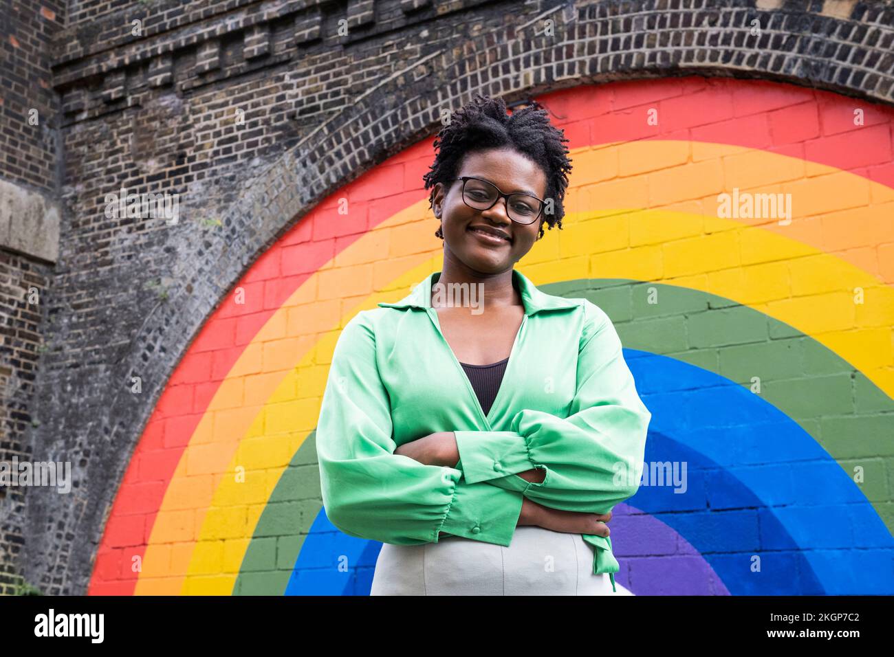 Jeune femme souriante aux bras croisés devant un mur de couleur arc-en-ciel Banque D'Images
