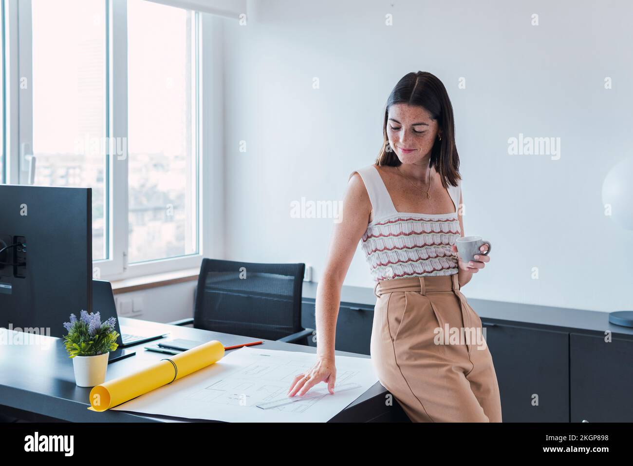 Jeune architecte regardant un plan tenant une tasse à café au bureau Banque D'Images